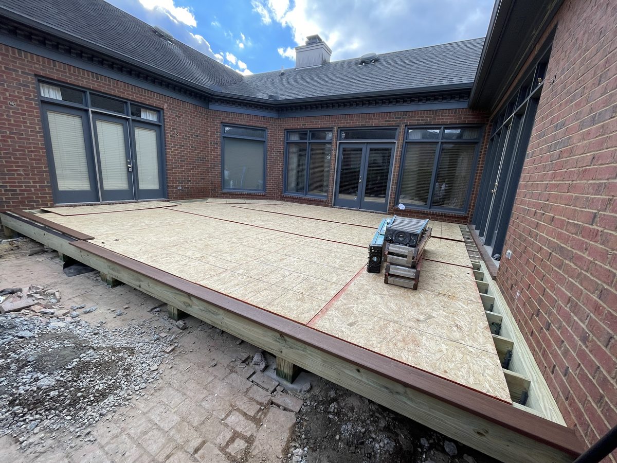 A large courtyard deck framed in treated lumber and sheathed, with a dark picture-frame border, wrapping a brick house