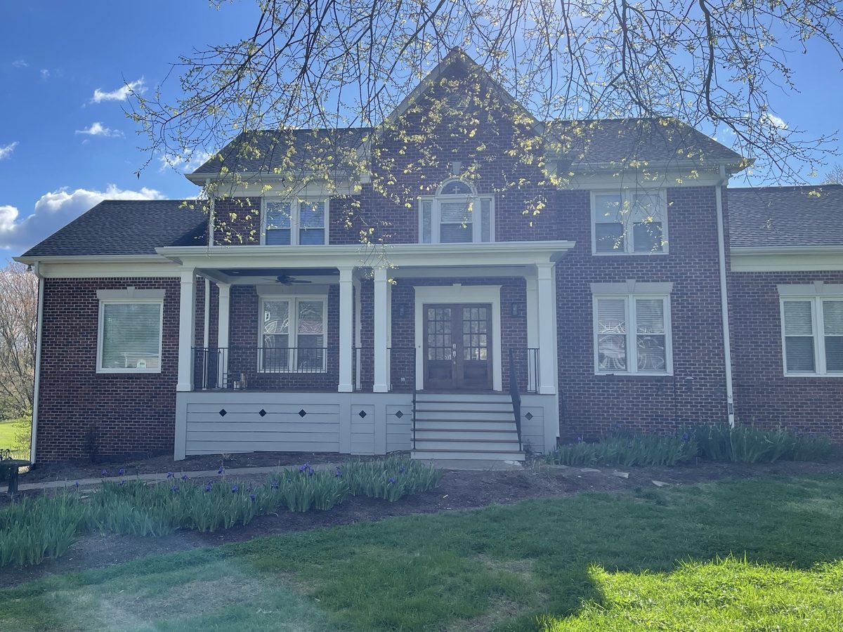 A covered front porch across a two-story brick home, with square white columns, black metal railings, white skirting with diamond cutouts and steps up to wood double doors