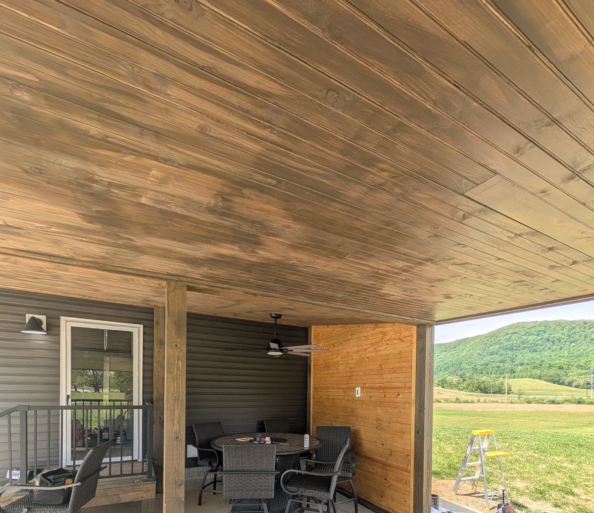 A covered patio with a stained tongue-and-groove ceiling, a knotty pine accent wall and a mountain view