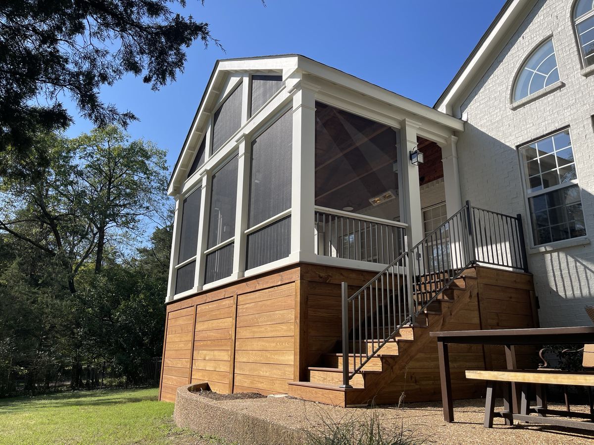 A finished gable screened porch with white trim and columns, stained wood skirting and stairs with metal railings, on a painted brick home
