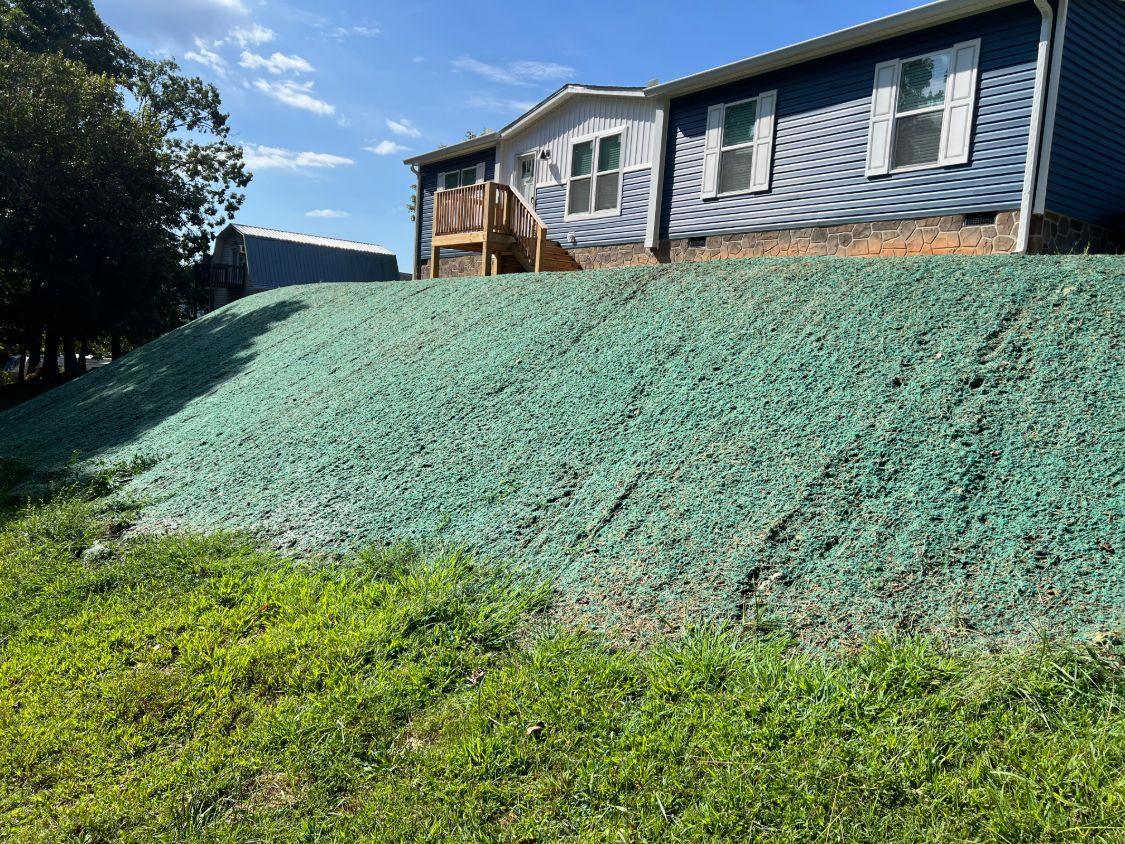 A steep slope below a house freshly hydroseeded, with wooden deck stairs above