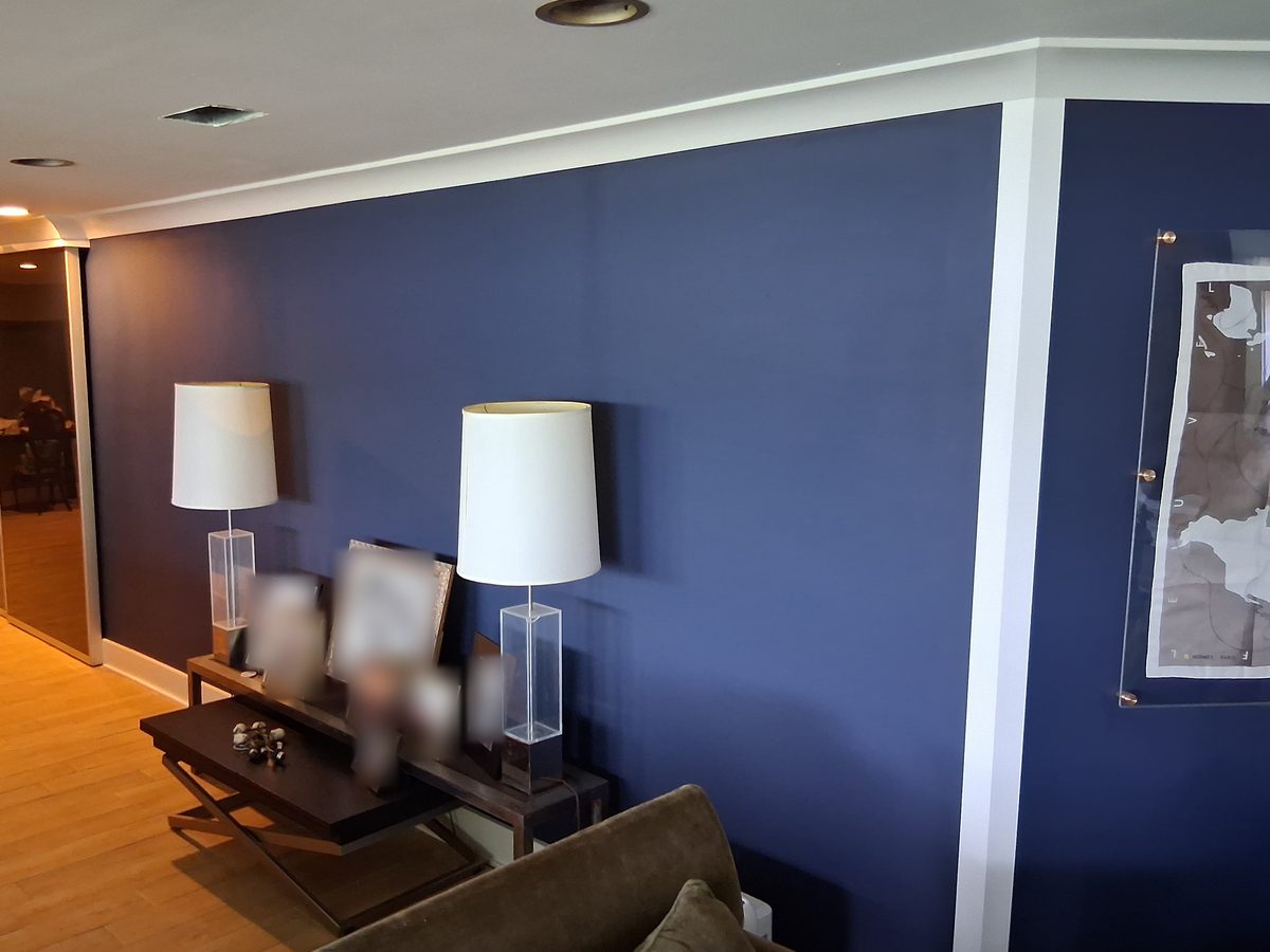 A living room wall painted deep navy with new white crown moulding, baseboard and vertical trim