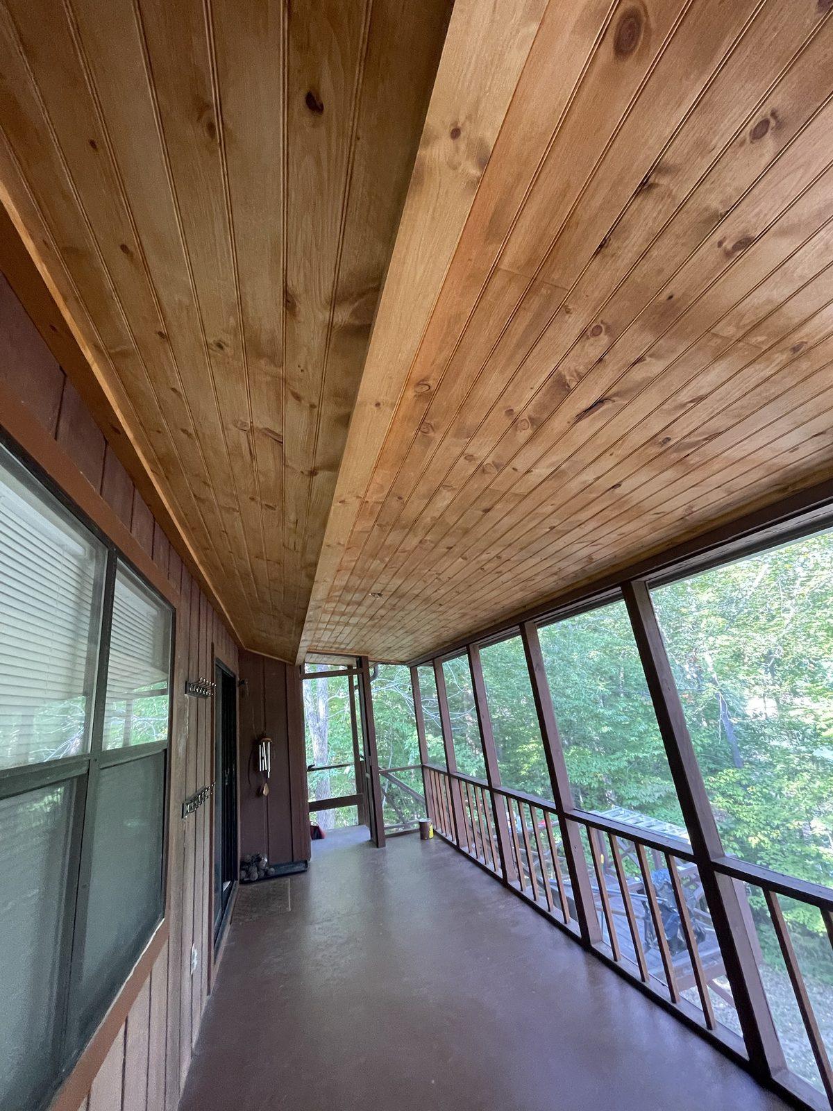 A long screened porch with a stained tongue-and-groove pine ceiling, looking out into the trees