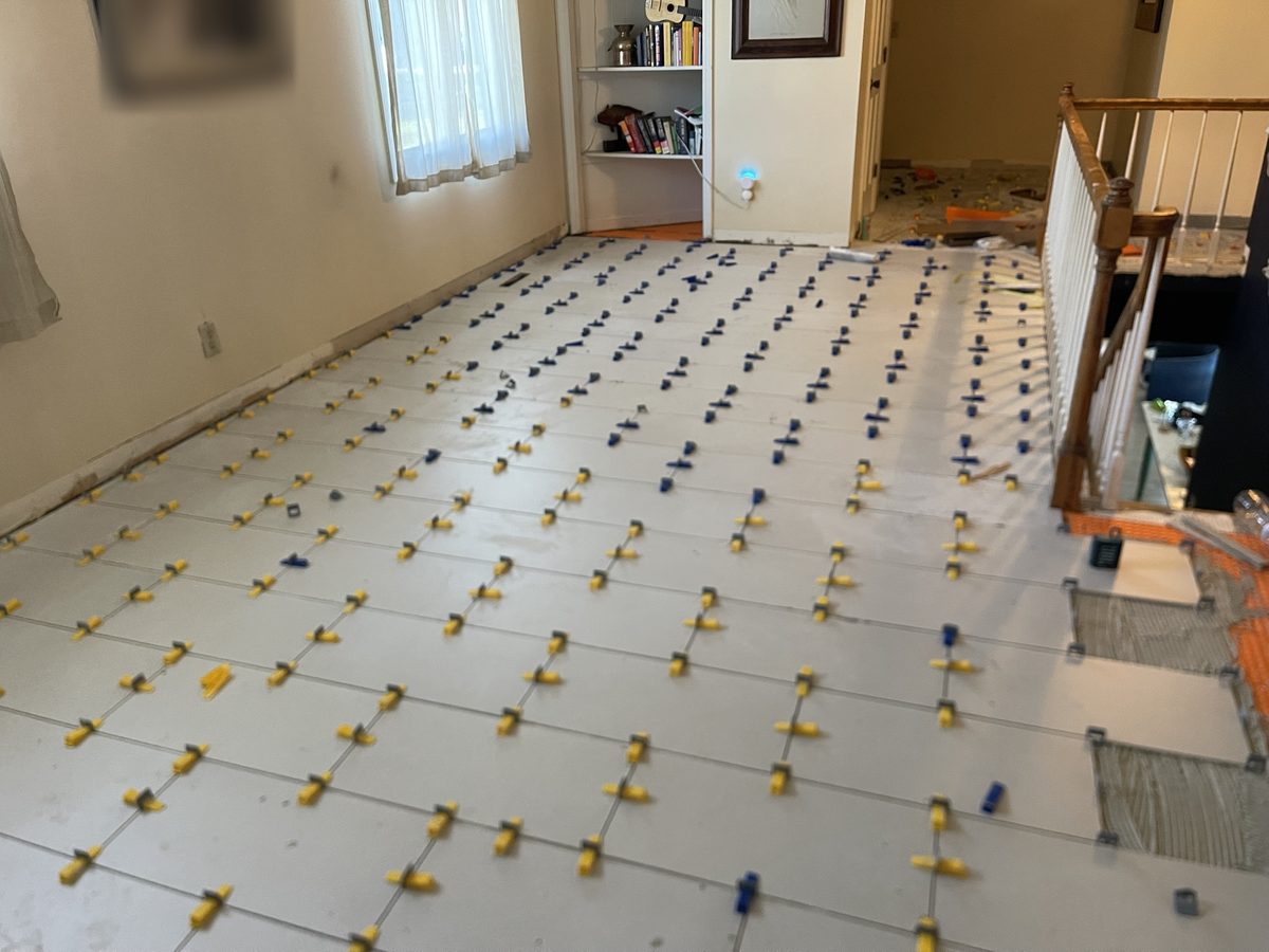 A large-format tile floor being set in an upstairs room, with leveling clips still in place